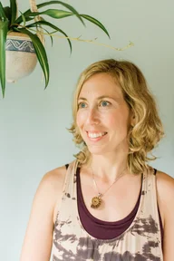 A person with shoulder-length blonde hair is smiling while looking away from the camera.