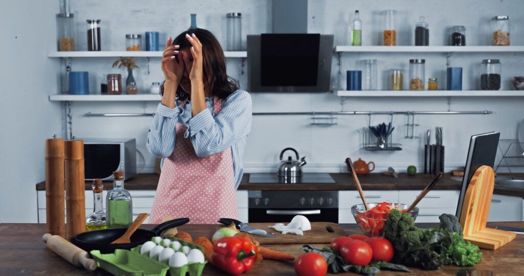 Woman wiping irritated eyes near chopped onion on chopping board in the kitchen