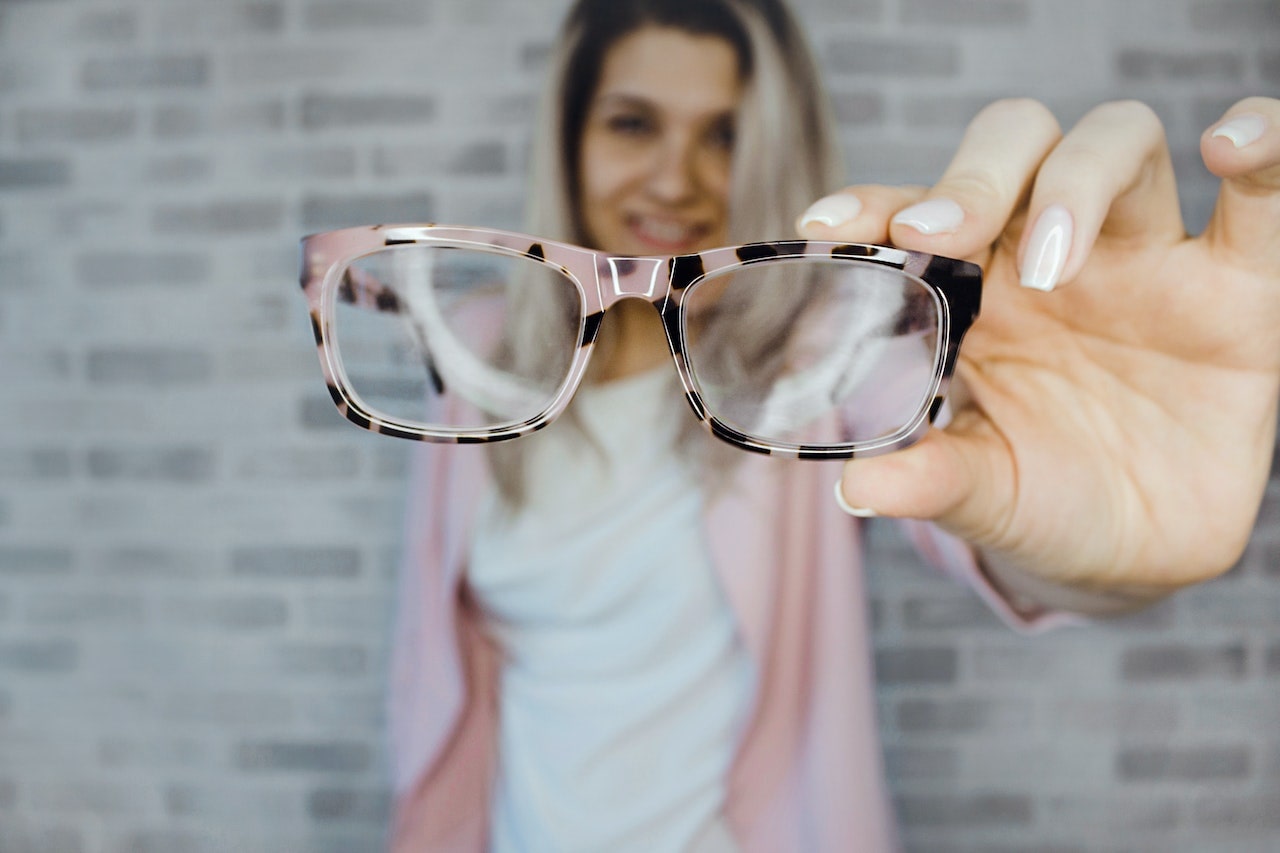 Woman with dyed hair holding up eyeglasses to focus