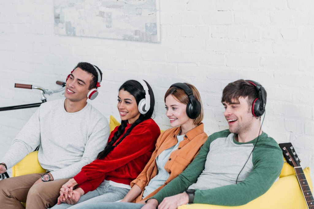 Multiethnic friends listening music with headphones while sitting together on a yellow couch